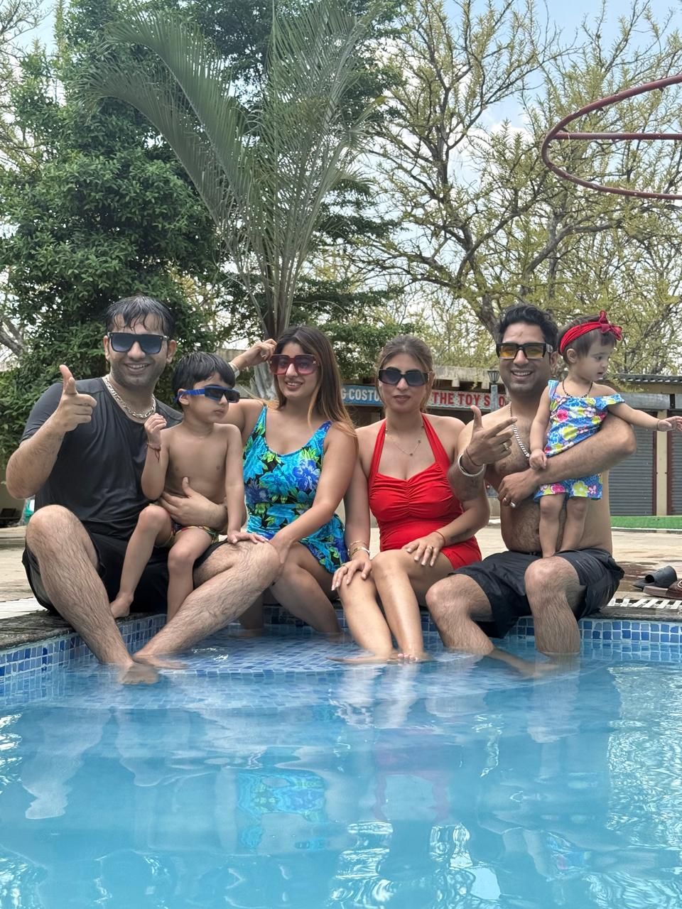 Families with children in swimwear sitting at the edge of the outdoor swimming pool during a day outing at Rangmanch Farms in Gurugram near Delhi