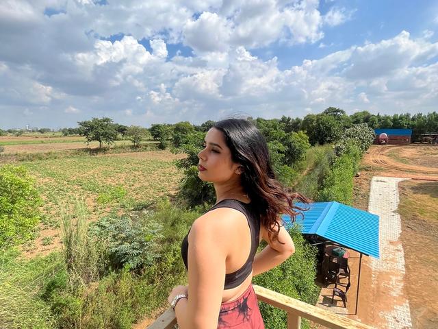 Woman standing at a wooden railing overlooking open fields and greenery under a blue sky at Rangmanch Farms, an outdoor day outing venue in Gurugram near Delhi