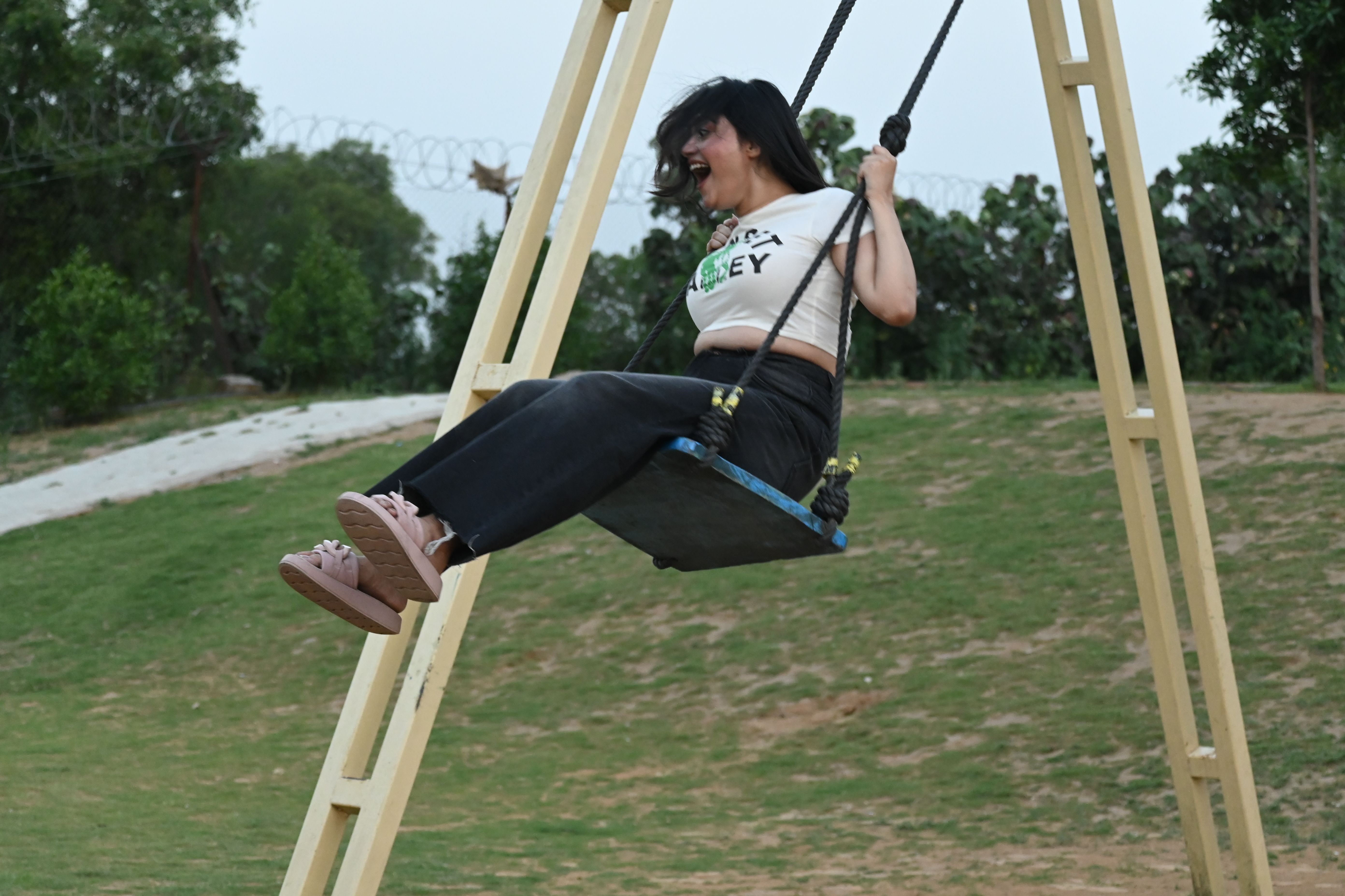 A guest laughing while swinging on an outdoor swing on the grassy field at Rangmanch Farms, a day outing venue in Gurugram near Delhi