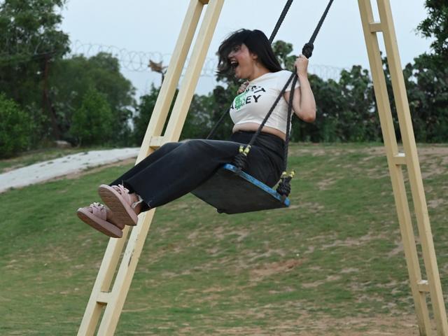 A guest laughing while swinging on an outdoor swing on the grassy field at Rangmanch Farms, a day outing venue in Gurugram near Delhi