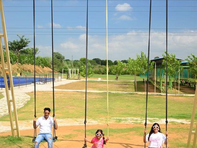A family sitting on outdoor rope swings on the open grounds with a pool and seating area behind at Rangmanch Farms, a family day outing venue in Gurugram near Delhi