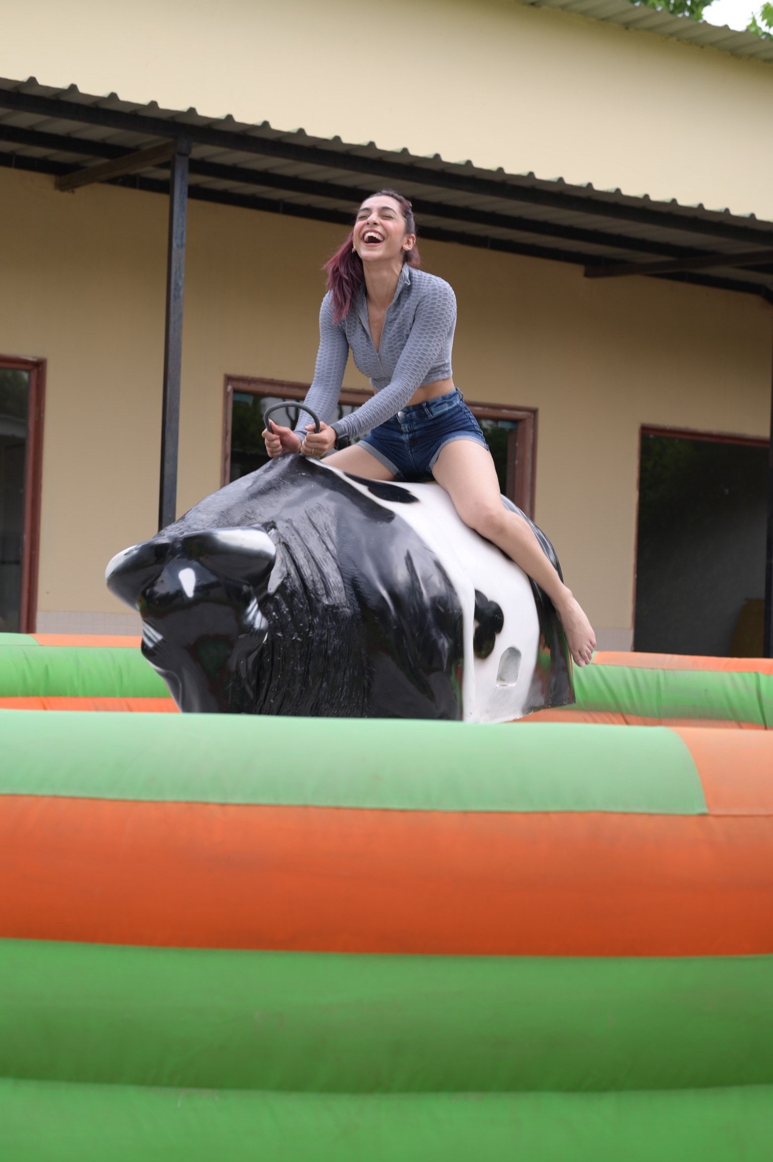 A woman laughing while riding the mechanical bull ride on an inflatable base at Rangmanch Farms, an outdoor day outing venue in Gurugram near Delhi