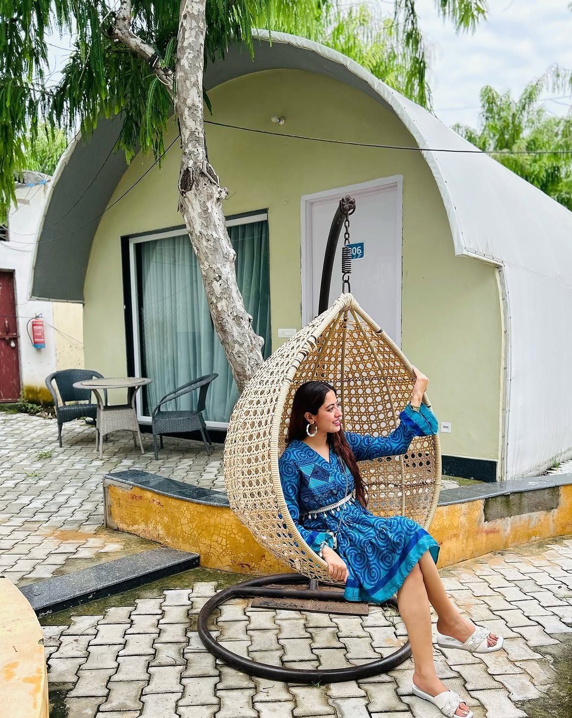 Woman seated in a woven hanging swing chair outside an arched dome cottage during an overnight stay at Rangmanch Farms, Gurugram near Delhi