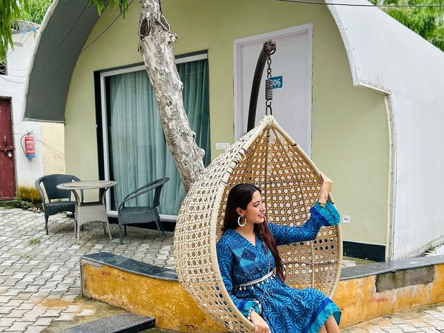Woman seated in a woven hanging swing chair outside an arched dome cottage during an overnight stay at Rangmanch Farms, Gurugram near Delhi