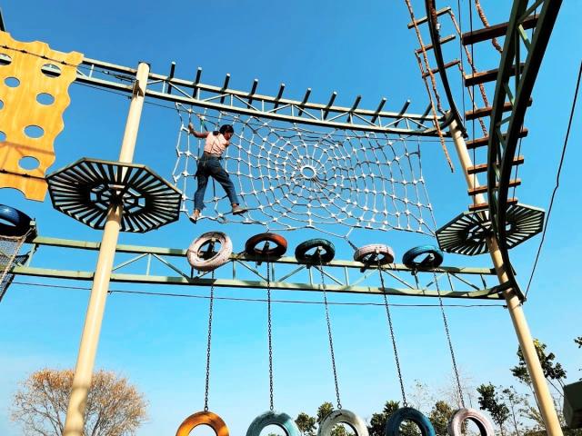 A person crossing a high rope net on the outdoor obstacle course with hanging tyres below at Rangmanch Farms, an adventure and team building venue in Gurugram near Delhi