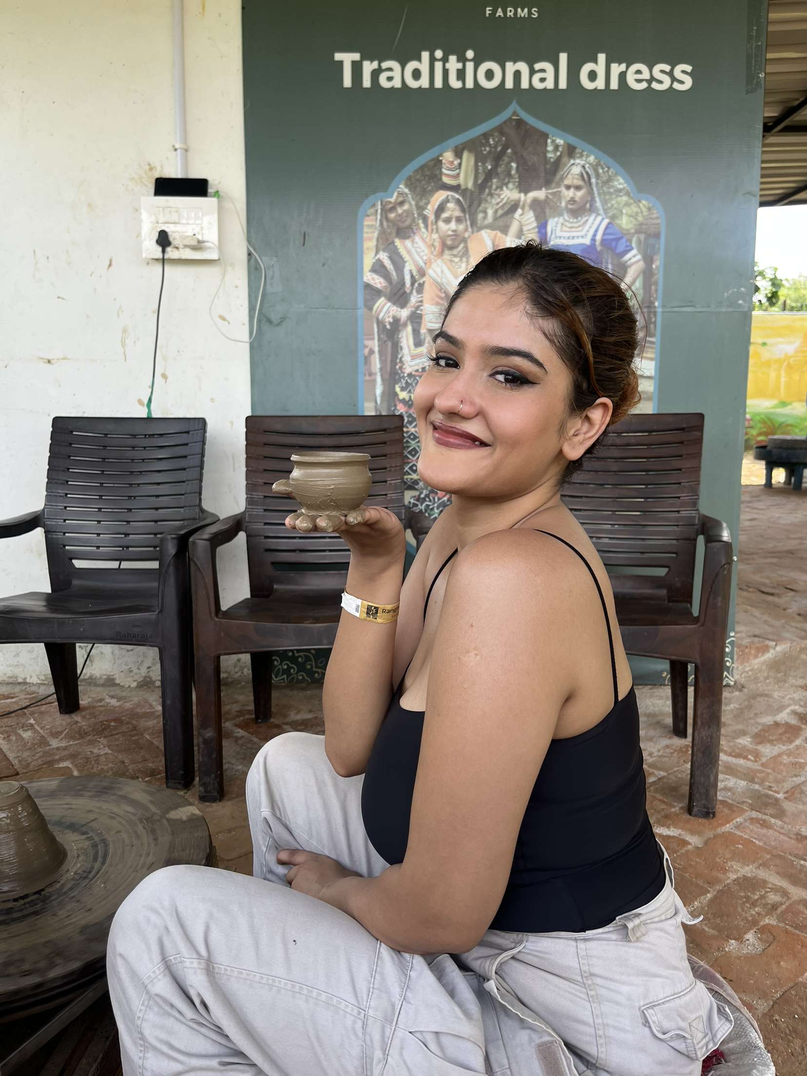 A guest holding a clay pot she made at a pottery activity, seated beside the pottery wheel at Rangmanch Farms, an outdoor day outing venue in Gurugram near Delhi