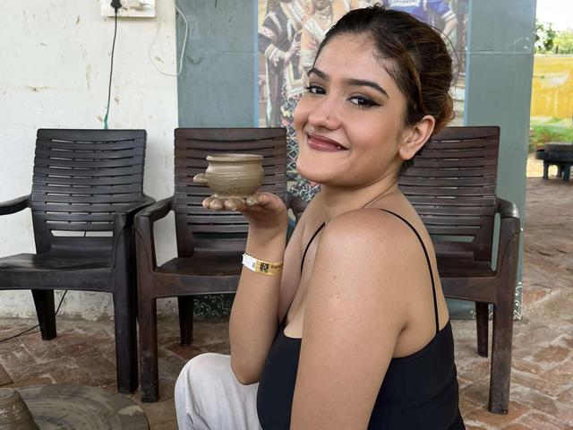 A guest holding a clay pot she made at a pottery activity, seated beside the pottery wheel at Rangmanch Farms, an outdoor day outing venue in Gurugram near Delhi