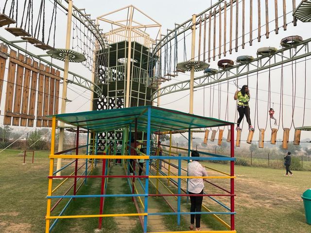 Participants harnessed on the elevated rope obstacle course with a colourful climbing structure below at Rangmanch Farms, an outdoor adventure and team building venue in Gurugram near Delhi