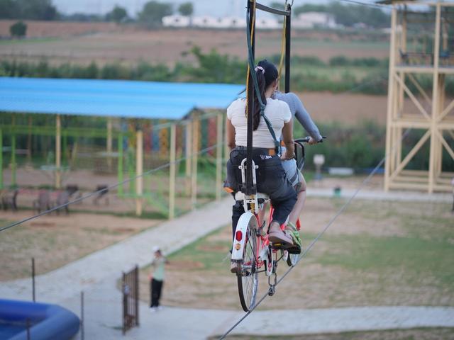 Two people riding a cycling zipline on a high rope across the outdoor adventure area at Rangmanch Farms, an outdoor day outing and team building venue in Gurugram near Delhi