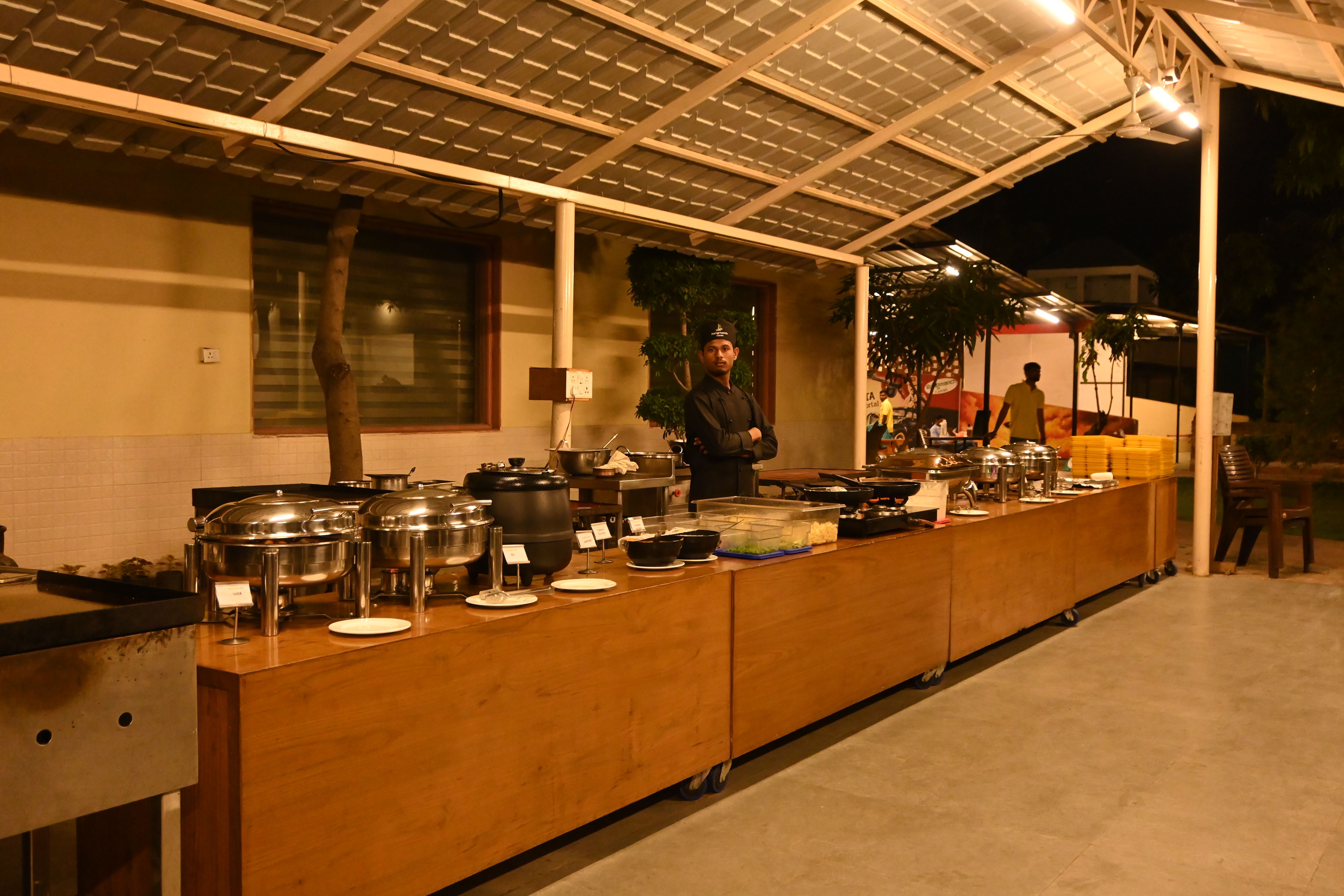 Staff attending a buffet counter with chafing dishes and a live counter during an evening dinner at Rangmanch Farms, an outdoor event venue in Gurugram near Delhi
