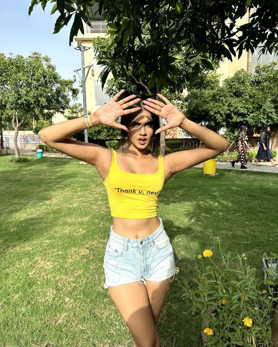 Woman in a yellow crop top and denim shorts posing on the grassy lawns with trees behind her at Rangmanch Farms, an outdoor day outing venue in Gurugram near Delhi