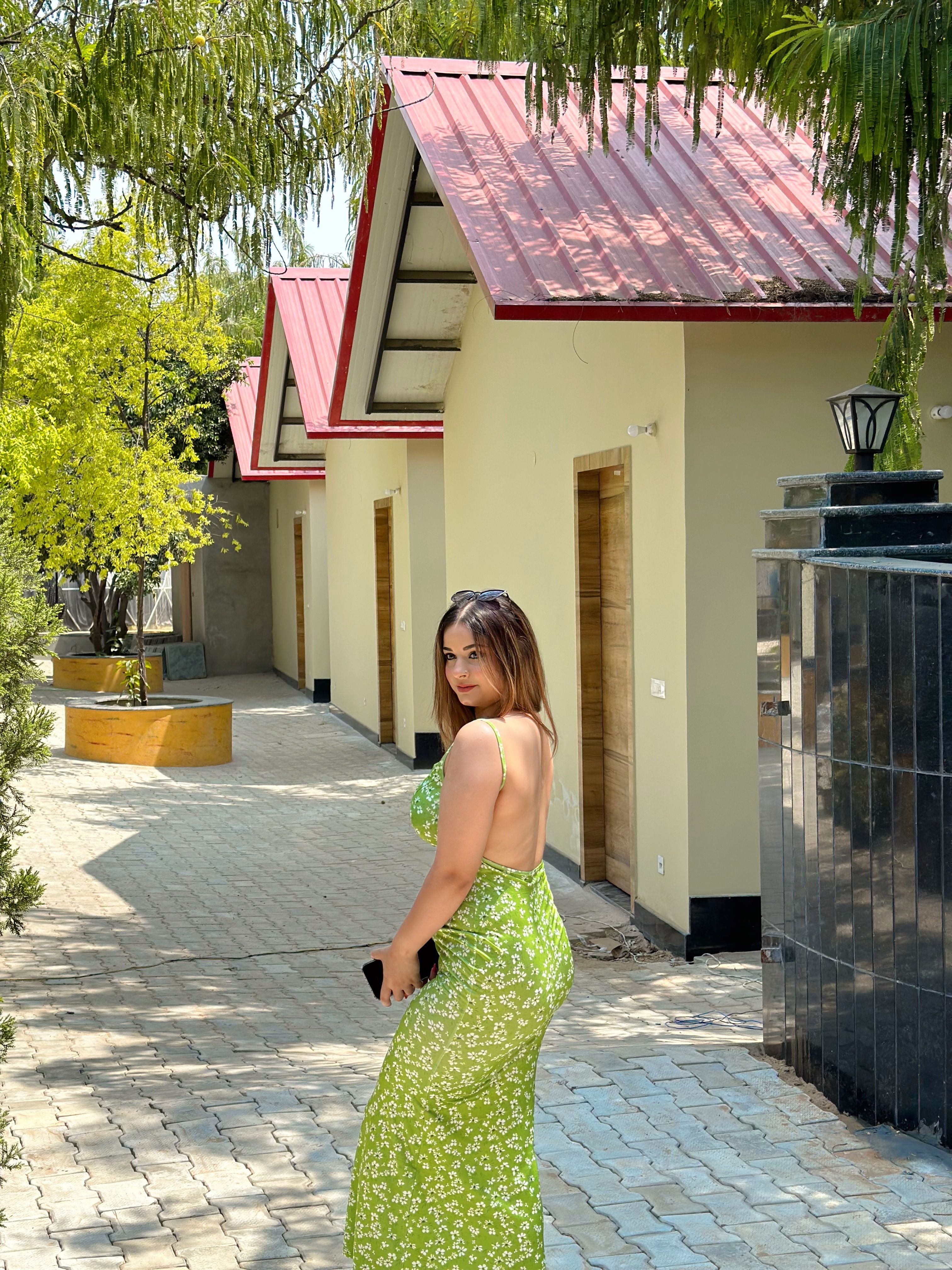 Woman in a green dress standing on the paved path beside red-roofed overnight stay cottages at Rangmanch Farms in Gurugram, near Delhi