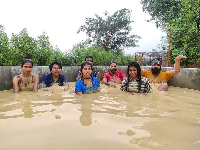A group enjoying the mud bath activity together with trees behind at Rangmanch Farms, an outdoor day outing venue in Gurugram near Delhi