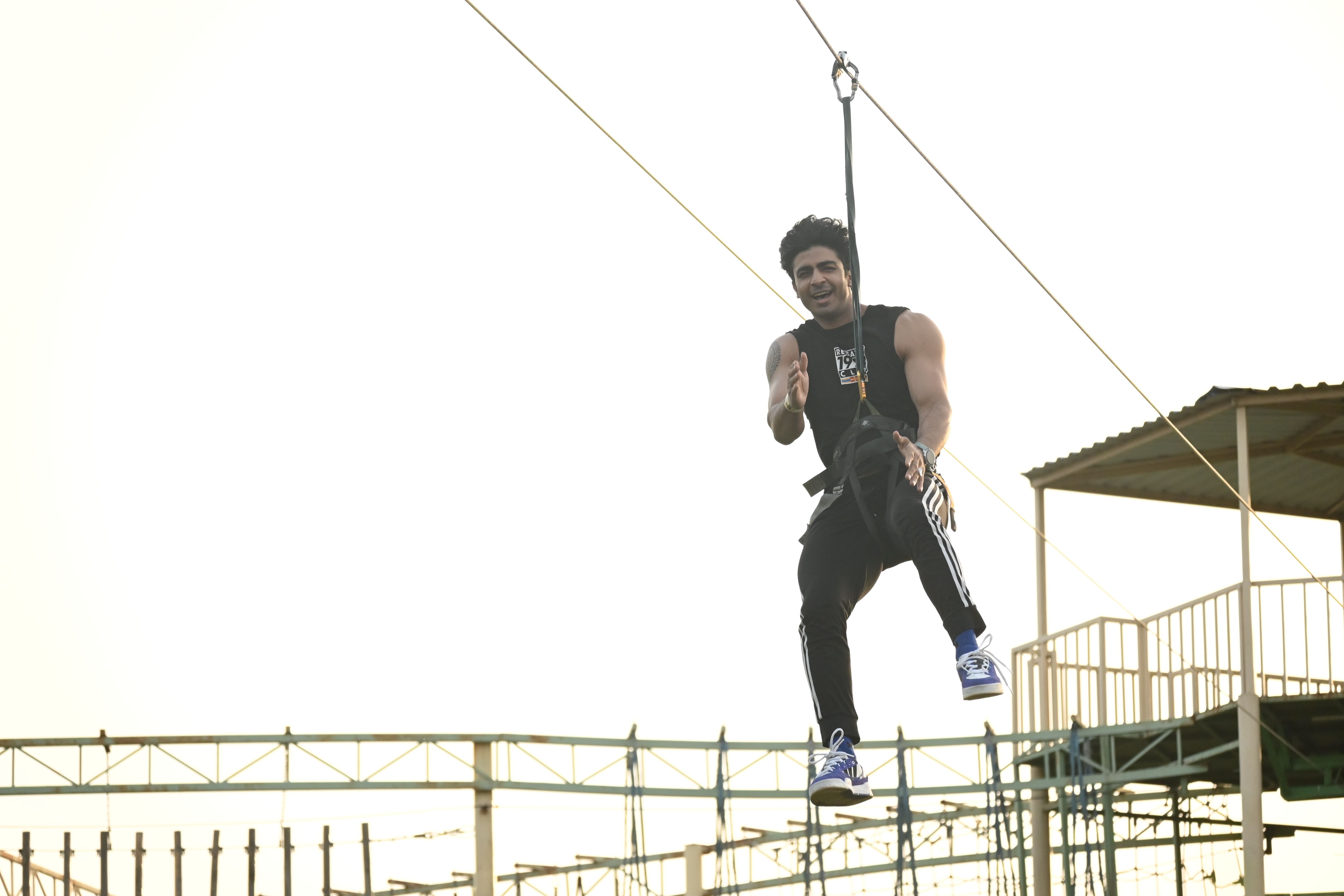 A man in a harness riding the zipline above the outdoor ropes course at Rangmanch Farms, an adventure activity venue for corporate outings in Gurugram near Delhi
