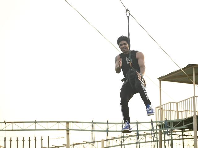 A man in a harness riding the zipline above the outdoor ropes course at Rangmanch Farms, an adventure activity venue for corporate outings in Gurugram near Delhi