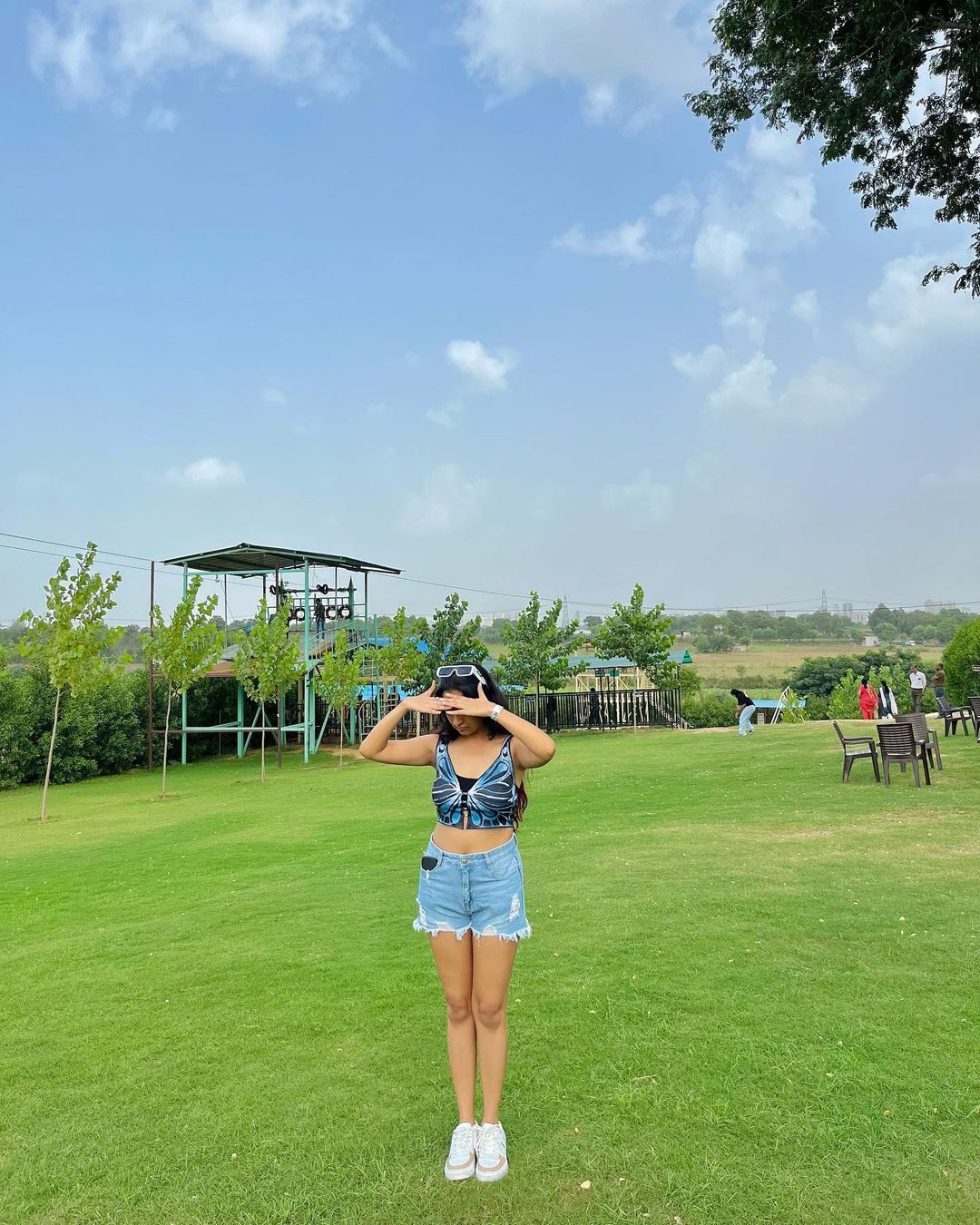 Woman standing on the open green lawn with an adventure obstacle tower behind her at Rangmanch Farms, an outdoor day outing venue in Gurugram near Delhi