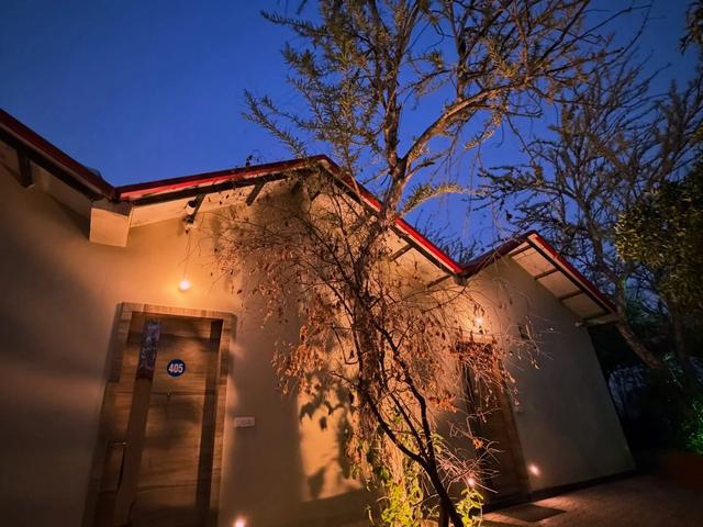 Numbered guest room entrances with wooden doors lit up in the evening beside a tree at Rangmanch Farms, an overnight stay venue in Gurugram near Delhi
