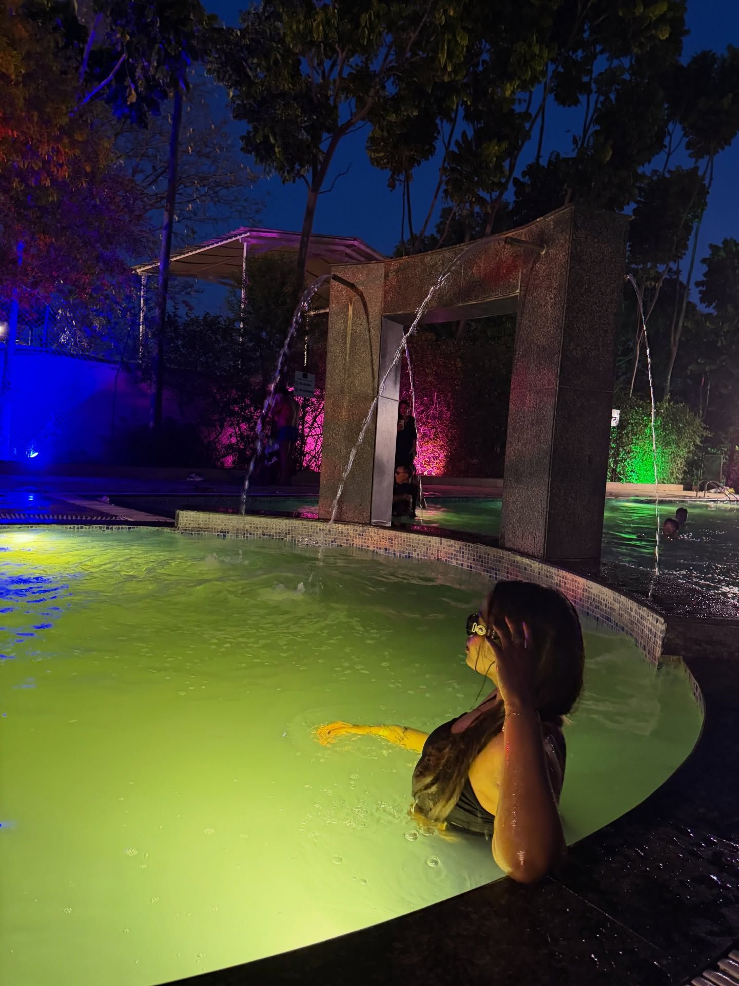 Guest relaxing in the illuminated swimming pool with water features at night during an evening outing at Rangmanch Farms in Gurugram, near Delhi