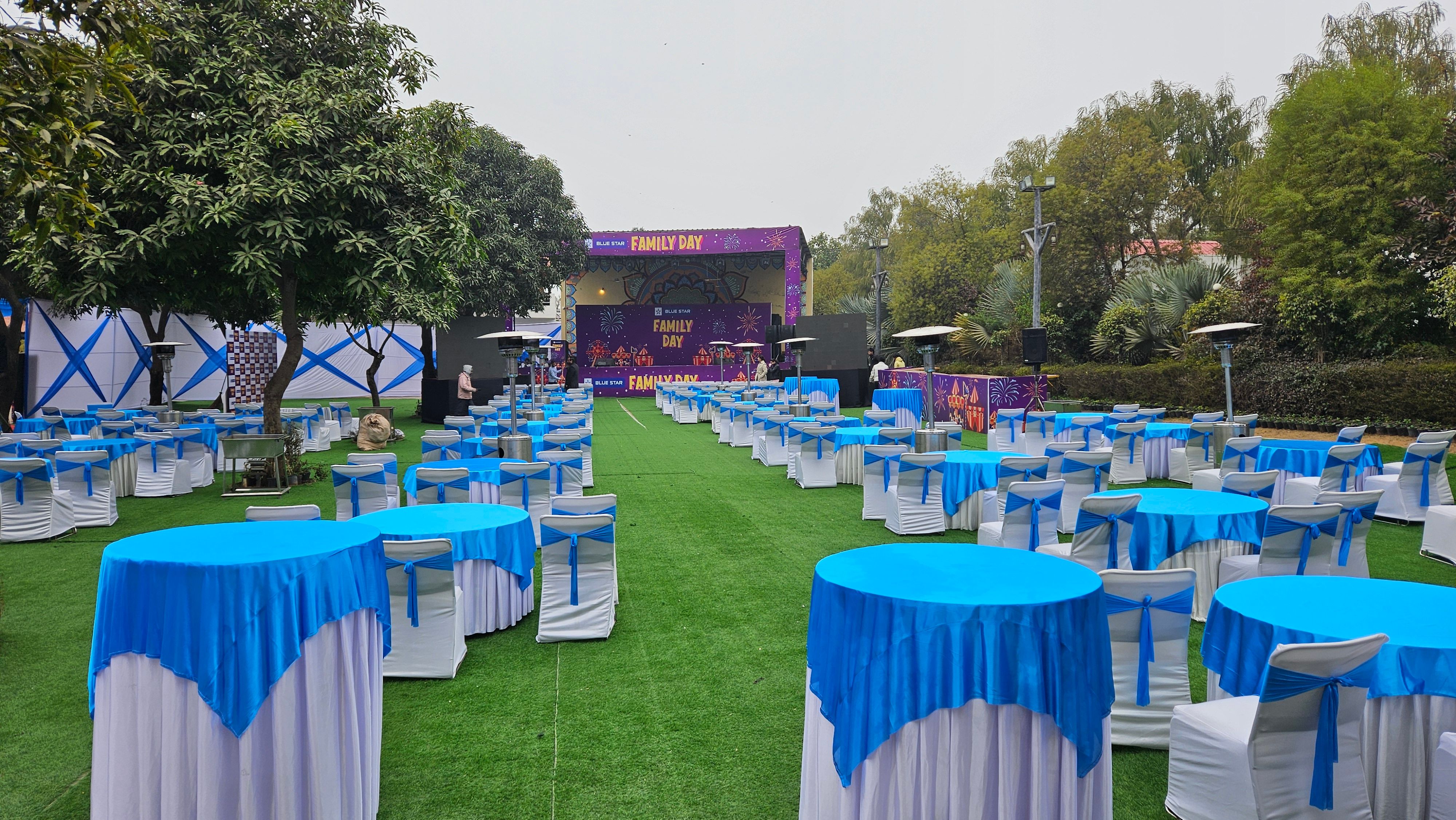 Corporate family day set-up with cocktail tables and an open-air stage on the lawn — corporate family day venue in Gurugram