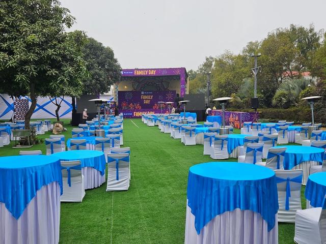 Corporate family day set-up with cocktail tables and an open-air stage on the lawn — corporate family day venue in Gurugram