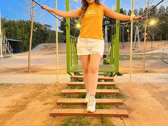 A woman crossing a wooden rope bridge on the outdoor adventure course at Rangmanch Farms, a day outing and team building venue in Gurugram near Delhi