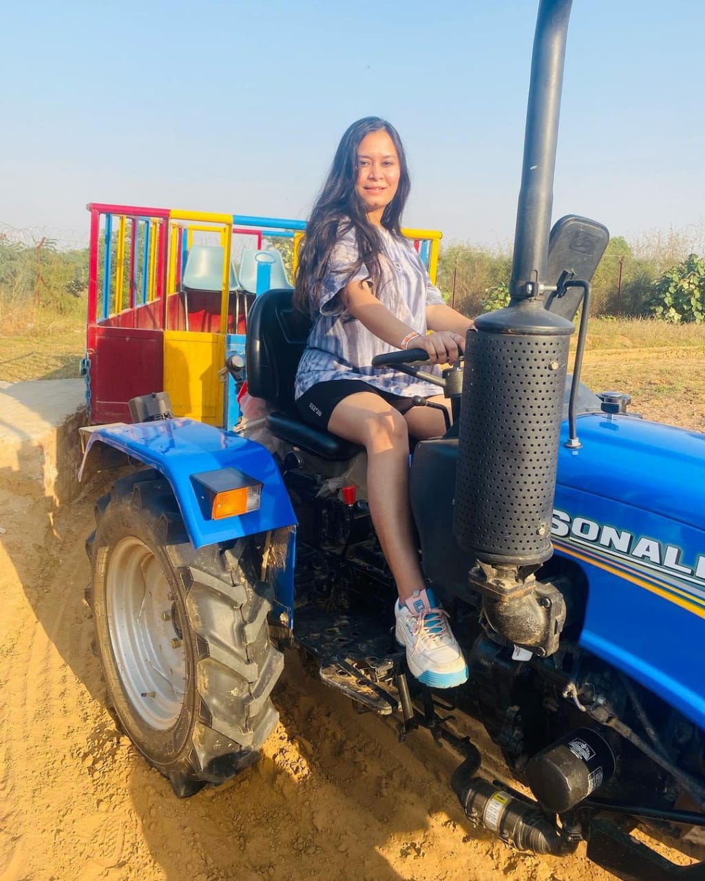 A woman seated on a blue tractor with a colourful trolley during a day outing at Rangmanch Farms, an outdoor venue in Gurugram near Delhi