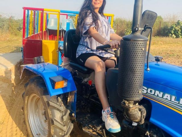A woman seated on a blue tractor with a colourful trolley during a day outing at Rangmanch Farms, an outdoor venue in Gurugram near Delhi
