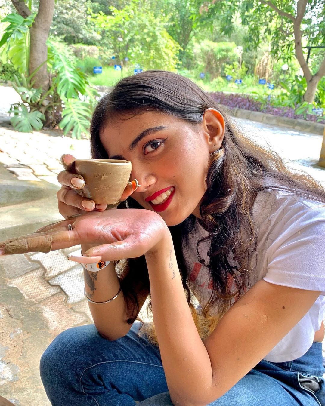Woman holding a clay cup she shaped at the pottery activity, with greenery behind her — day outing and activity venue at Rangmanch Farms in Gurugram, near Delhi