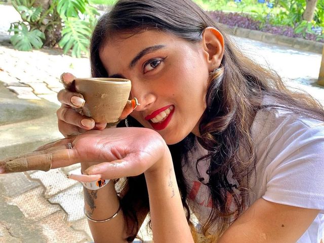 Woman holding a clay cup she shaped at the pottery activity, with greenery behind her — day outing and activity venue at Rangmanch Farms in Gurugram, near Delhi