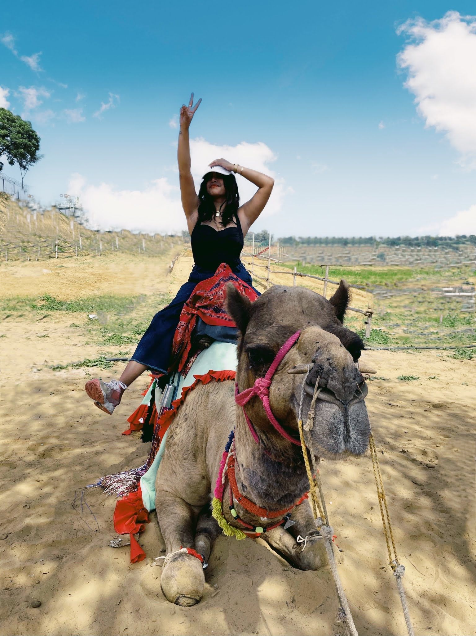 Woman posing on a decorated seated camel during a camel ride at Rangmanch Farms, an outdoor day outing venue in Gurugram near Delhi