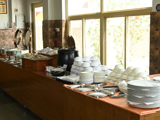 Indoor buffet counter with chafing dishes, stacked plates, bowls and cutlery laid out for an event at Rangmanch Farms in Gurugram, near Delhi