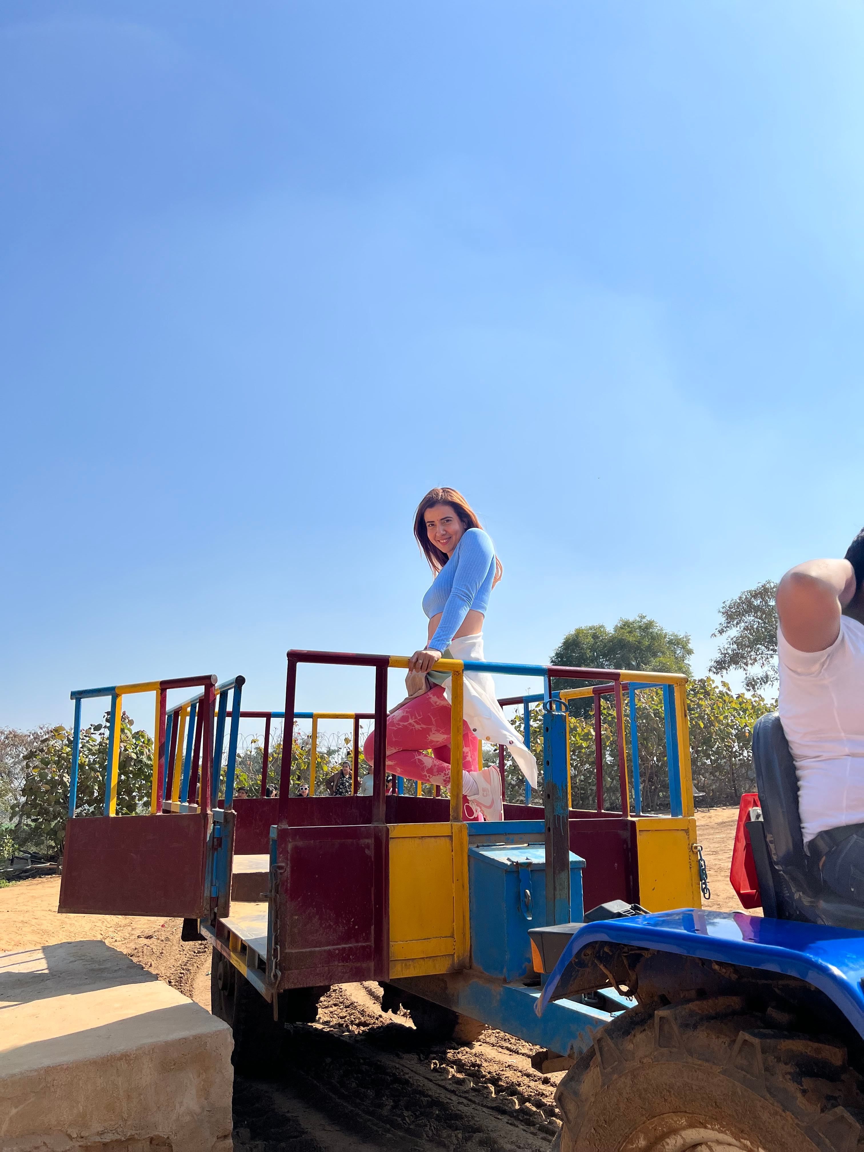 A woman boarding a colourful tractor trolley ride under a clear sky during a day outing at Rangmanch Farms in Gurugram, near Delhi