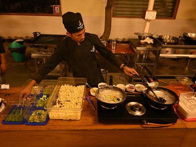 Chef preparing pasta at a live cooking counter with fresh vegetables and pans during an event at Rangmanch Farms, an outdoor venue in Gurugram near Delhi