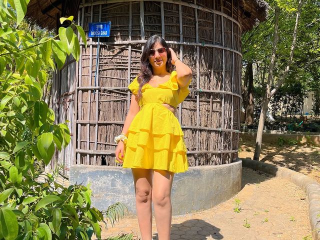 Woman in a yellow dress posing beside a round thatched mud hut surrounded by greenery at Rangmanch Farms, an outdoor day outing venue in Gurugram near Delhi
