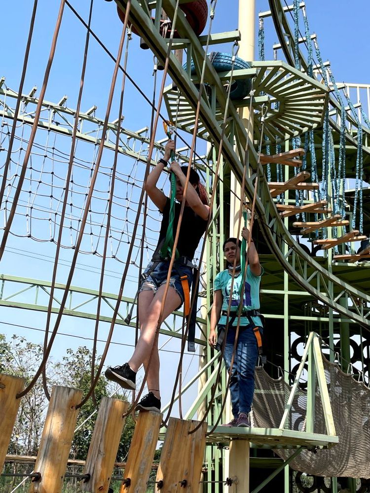 Two people in safety harnesses crossing the high ropes obstacle course during an outdoor adventure activity at Rangmanch Farms in Gurugram, near Delhi
