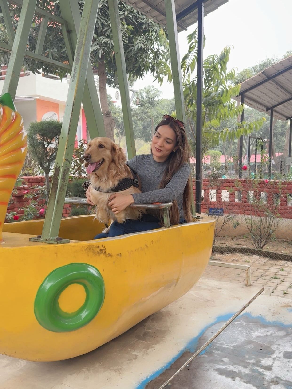 Woman sitting with a golden retriever in a yellow boat-shaped swing ride during a pet-friendly day outing at Rangmanch Farms, an outdoor venue in Gurugram near Delhi
