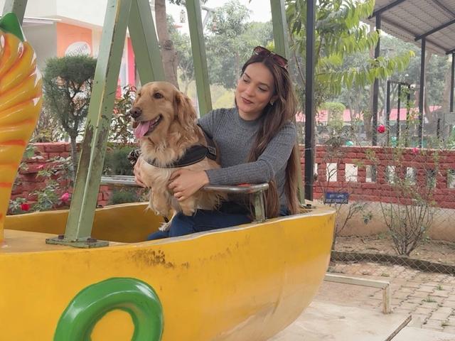 Woman sitting with a golden retriever in a yellow boat-shaped swing ride during a pet-friendly day outing at Rangmanch Farms, an outdoor venue in Gurugram near Delhi