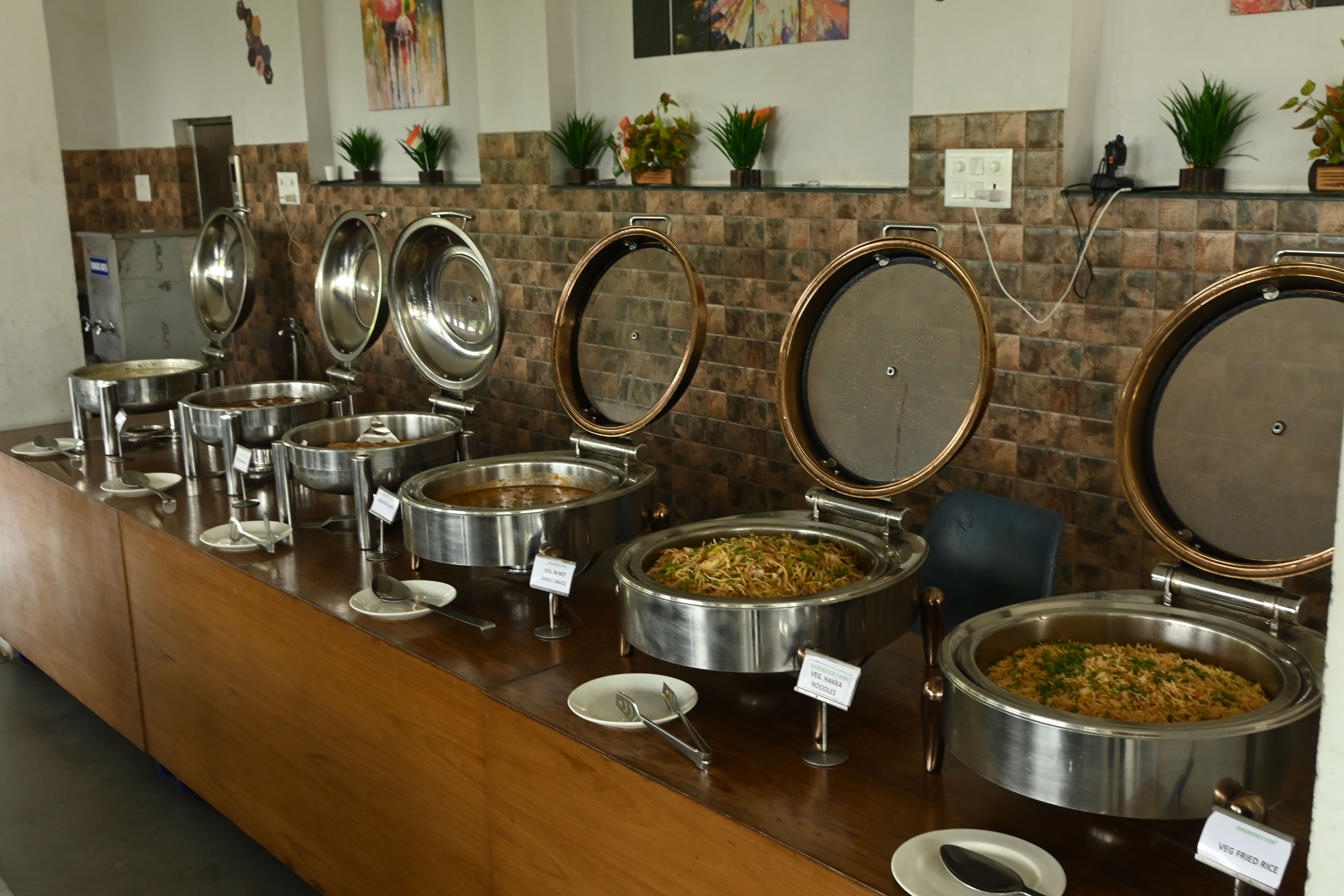 Chafing dishes with main course laid out on a wooden buffet counter at Rangmanch Farms, an outing and event venue in Gurugram near Delhi