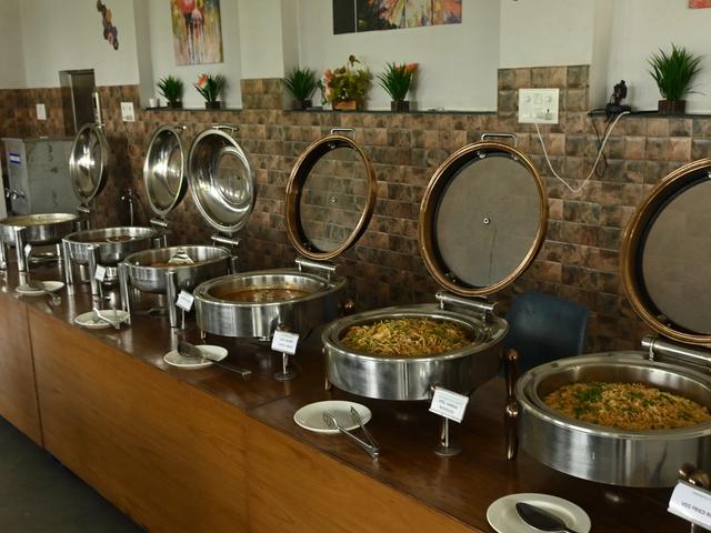Chafing dishes with main course laid out on a wooden buffet counter at Rangmanch Farms, an outing and event venue in Gurugram near Delhi