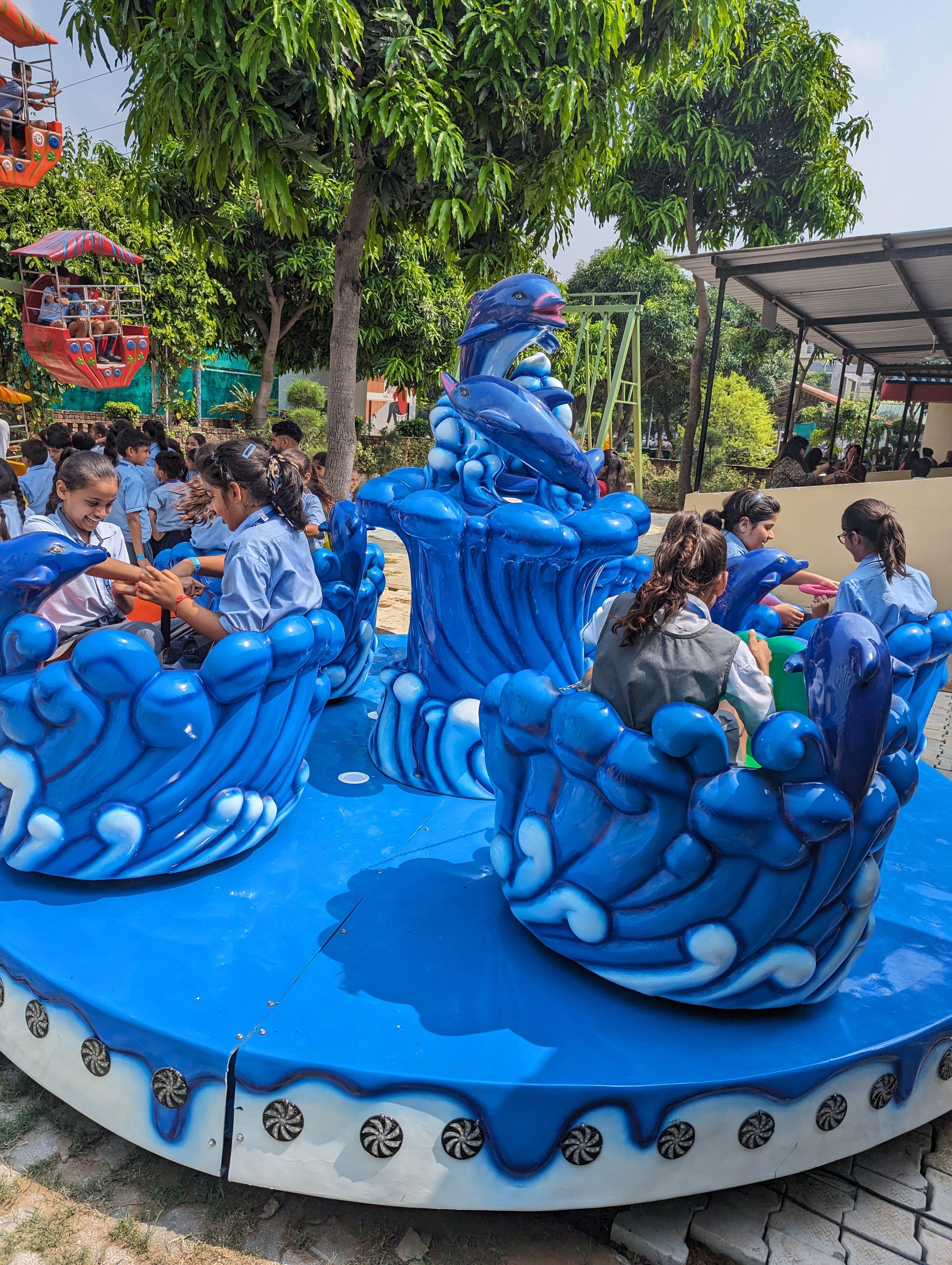 School children in uniform seated on a blue dolphin-themed spinning ride during a school trip at Rangmanch Farms in Gurugram, near Delhi