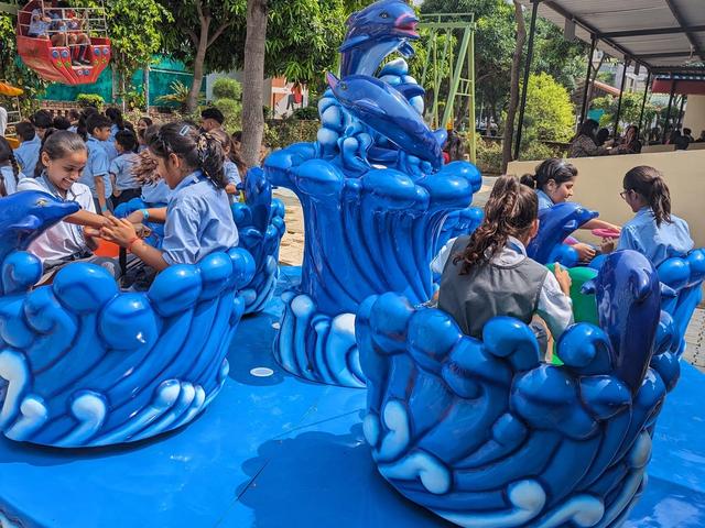 School children in uniform seated on a blue dolphin-themed spinning ride during a school trip at Rangmanch Farms in Gurugram, near Delhi
