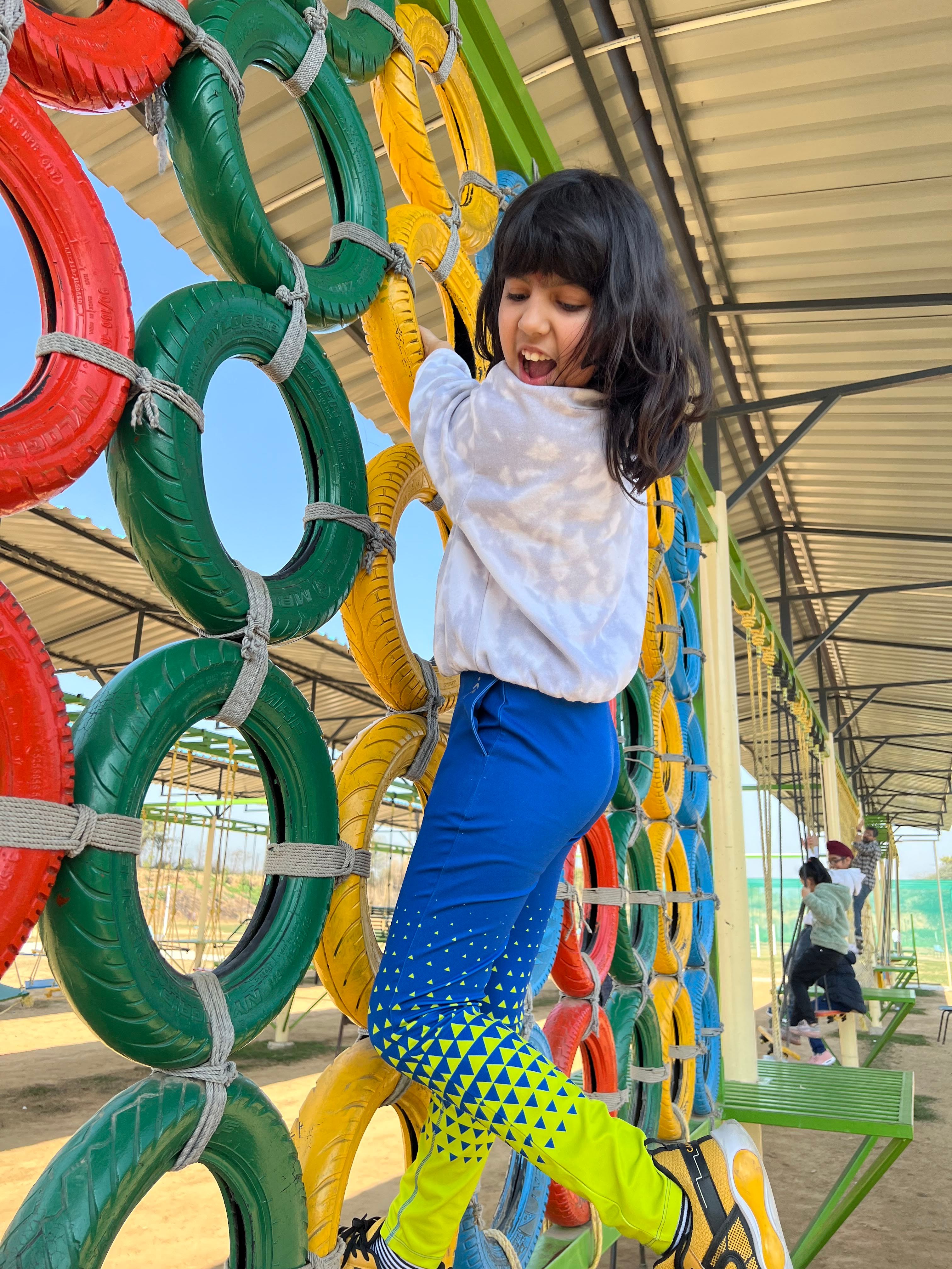 A child climbing a colourful tyre wall on the outdoor adventure course at Rangmanch Farms, a school trip and day outing venue in Gurugram near Delhi