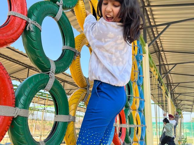 A child climbing a colourful tyre wall on the outdoor adventure course at Rangmanch Farms, a school trip and day outing venue in Gurugram near Delhi