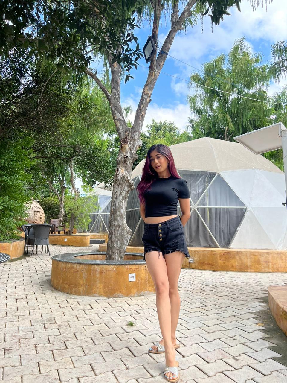 Woman in black outfit standing on a paved courtyard beside geodesic glamping domes and shady trees at Rangmanch Farms, an overnight stay venue in Gurugram near Delhi