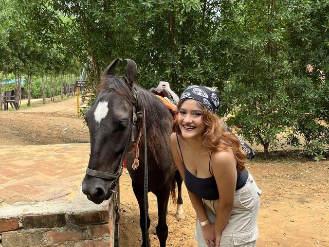 A smiling guest posing beside a saddled horse under shady trees during a day outing at Rangmanch Farms in Gurugram, near Delhi