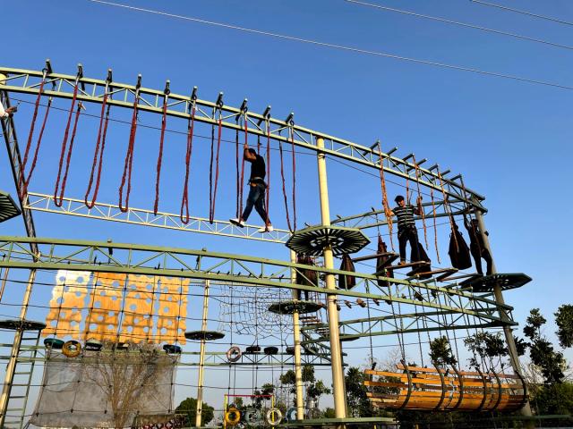 Participants crossing an elevated high ropes obstacle course against a clear sky at Rangmanch Farms, an outdoor adventure and team building venue in Gurugram near Delhi