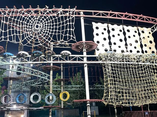 Outdoor rope and net obstacle course with hanging tyres lit up at night at Rangmanch Farms, an adventure and team building venue in Gurugram near Delhi