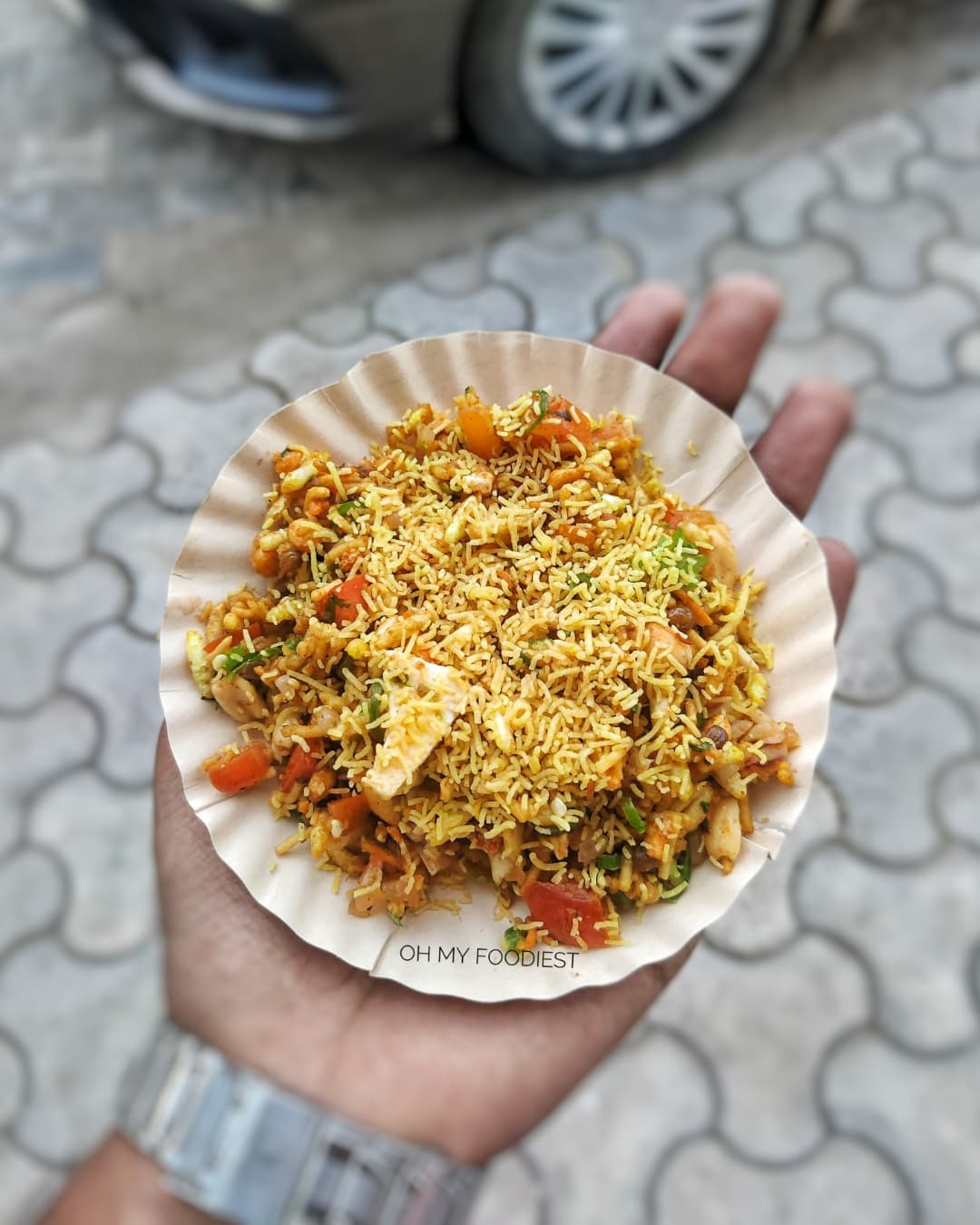A hand holding a paper plate of bhel from the chaat counter at Rangmanch Farms, an outdoor event venue in Gurugram near Delhi