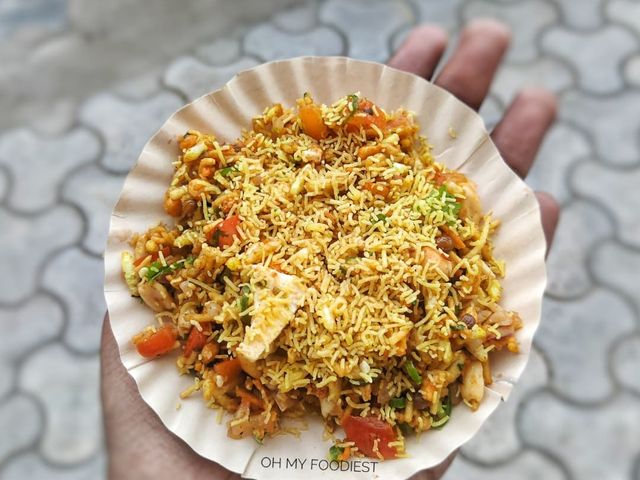 A hand holding a paper plate of bhel from the chaat counter at Rangmanch Farms, an outdoor event venue in Gurugram near Delhi
