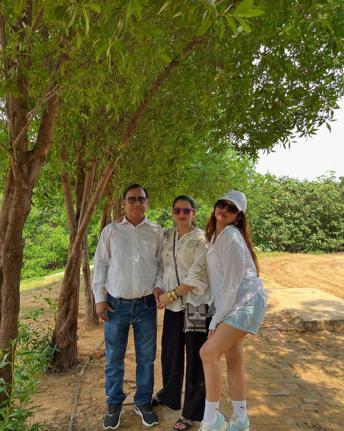 A family in white posing under a shady tree during a day outing at Rangmanch Farms, an outdoor venue in Gurugram near Delhi